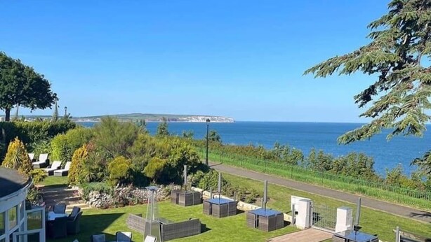 A patio with outdoor seating, a view of the sea, and a pathway leading to a building. - The Brunswick (Shanklin)