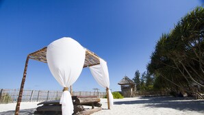 A beach setting with a wooden gazebo, white drapes, and a thatched-roof structure.