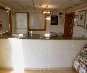 A reception area with a marble counter, a chandelier, a window with blinds, a bulletin board, and a door.