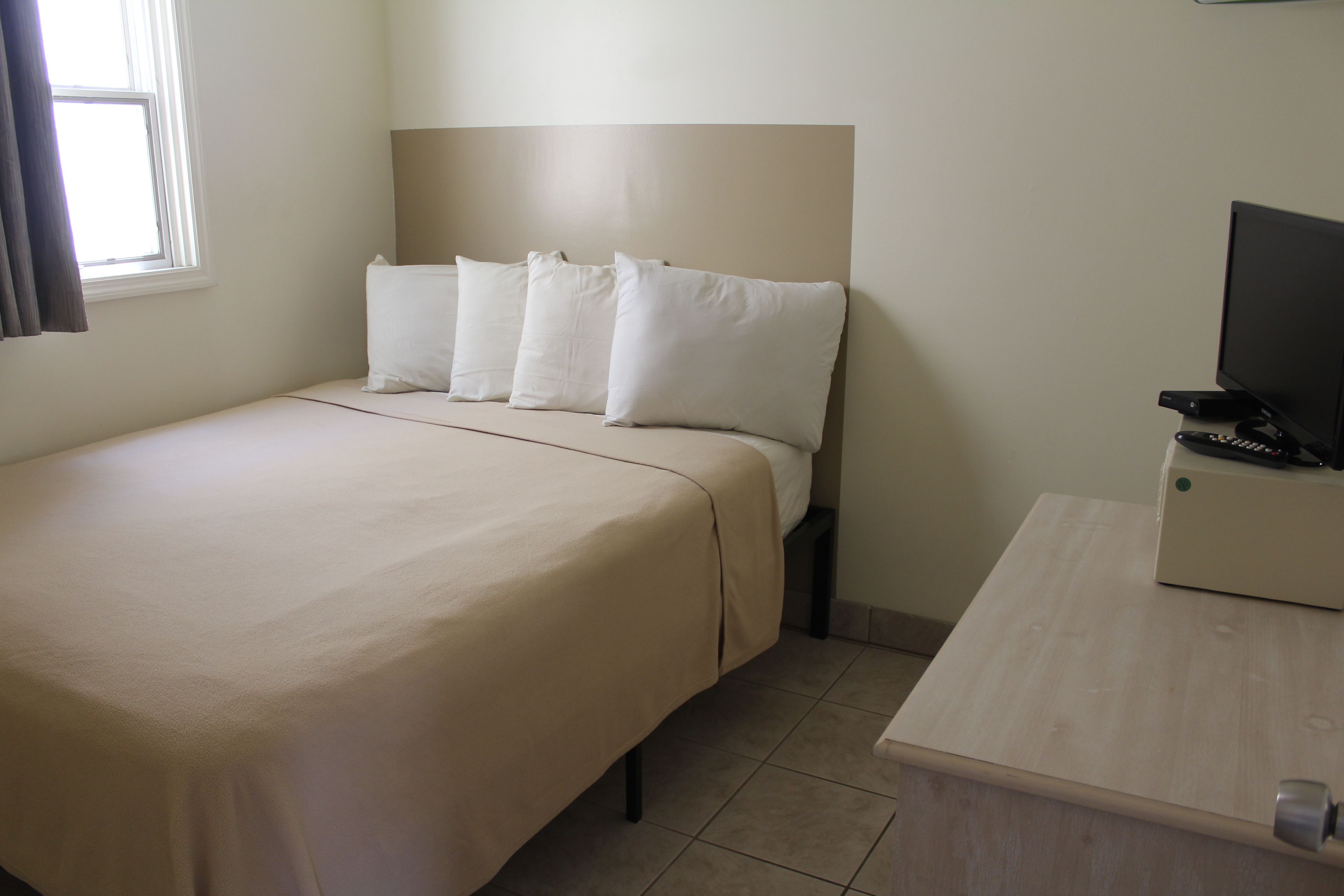 Una habitación de hotel con cama, televisión sobre una mesa de madera y ventana con cortinas.