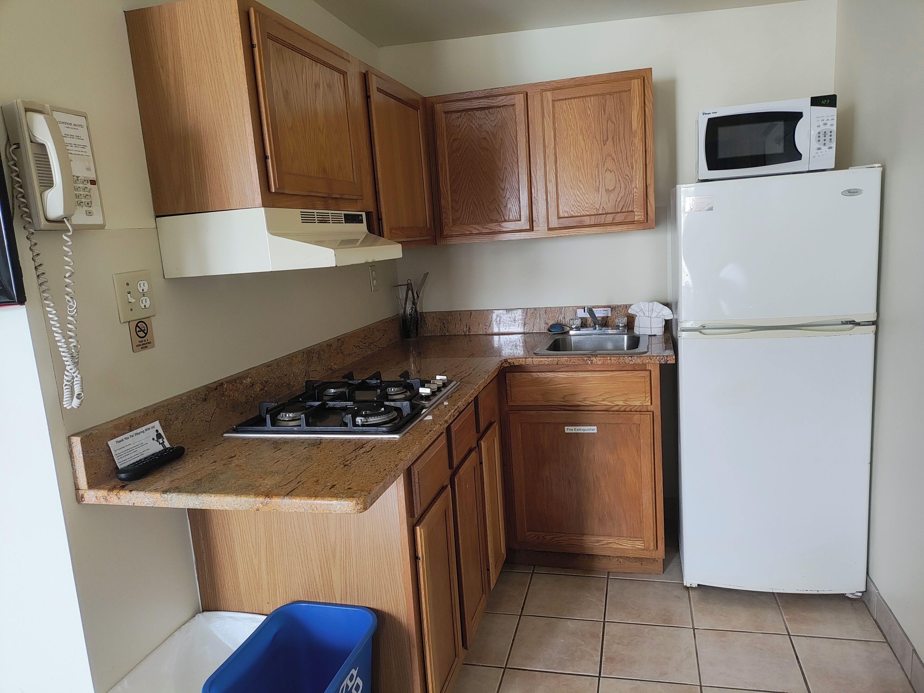 A compact kitchen with wooden cabinets, a gas stove, a microwave, and a refrigerator.