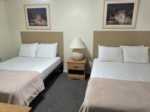 A hotel room with two beds, a nightstand with a lamp, and two framed pictures on the wall.