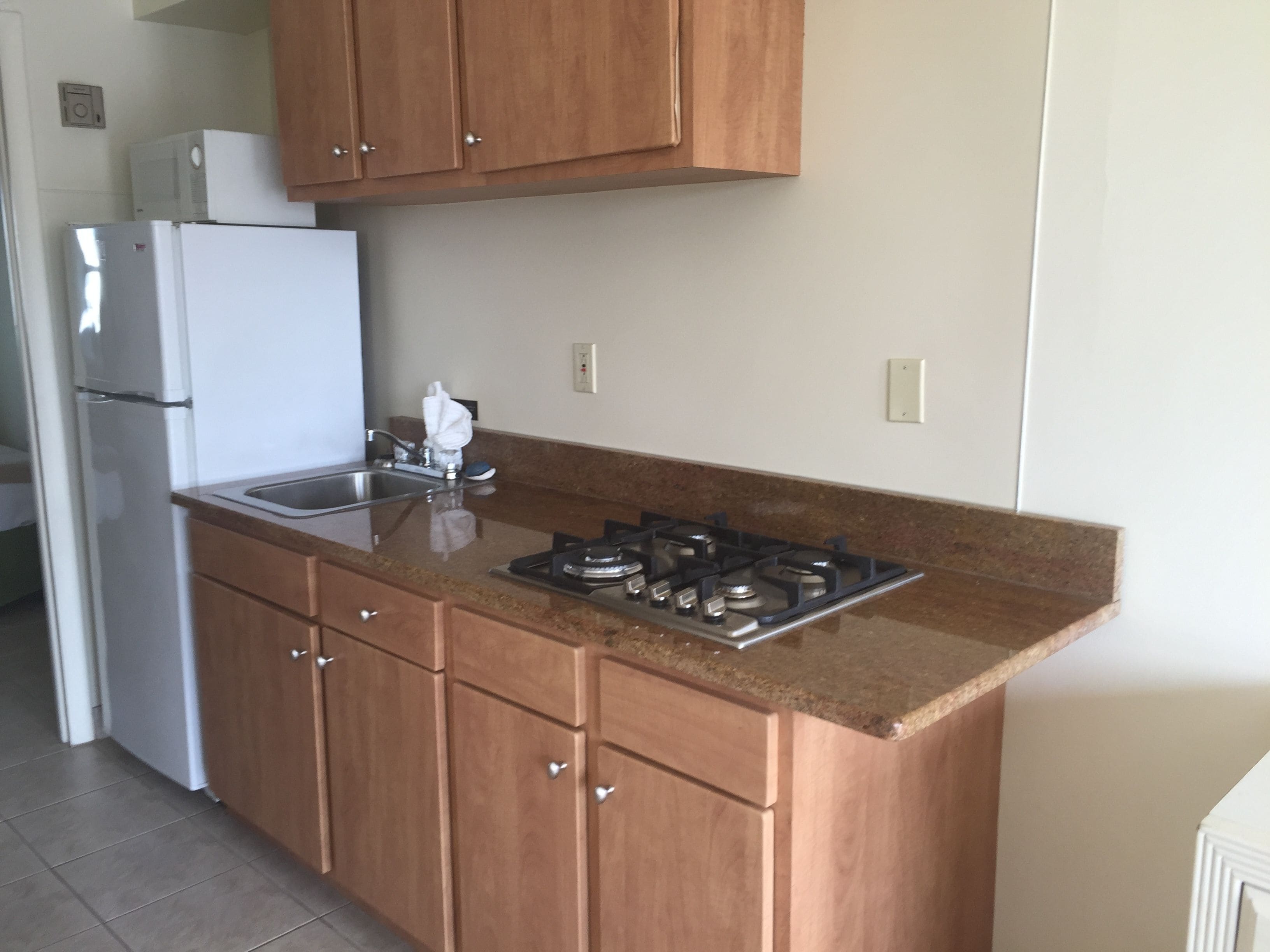 Una cocina con armarios de madera, un lavamanos de acero inoxidable, una estufa a gas y un refrigerador blanco.