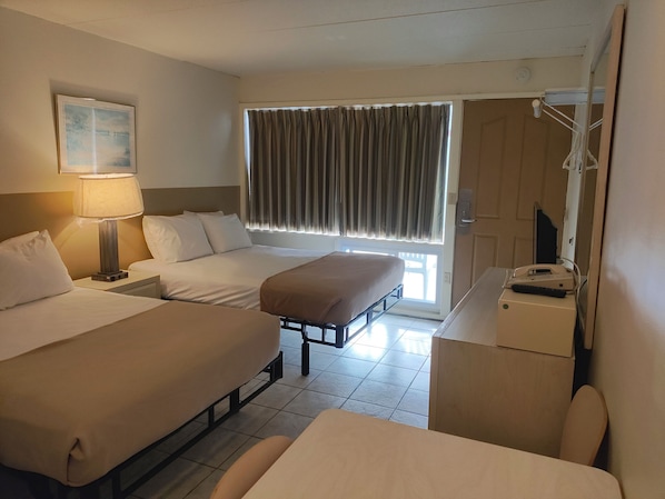 Una habitación de hotel con dos camas, un escritorio con teléfono, una lámpara y una ventana con cortinas.