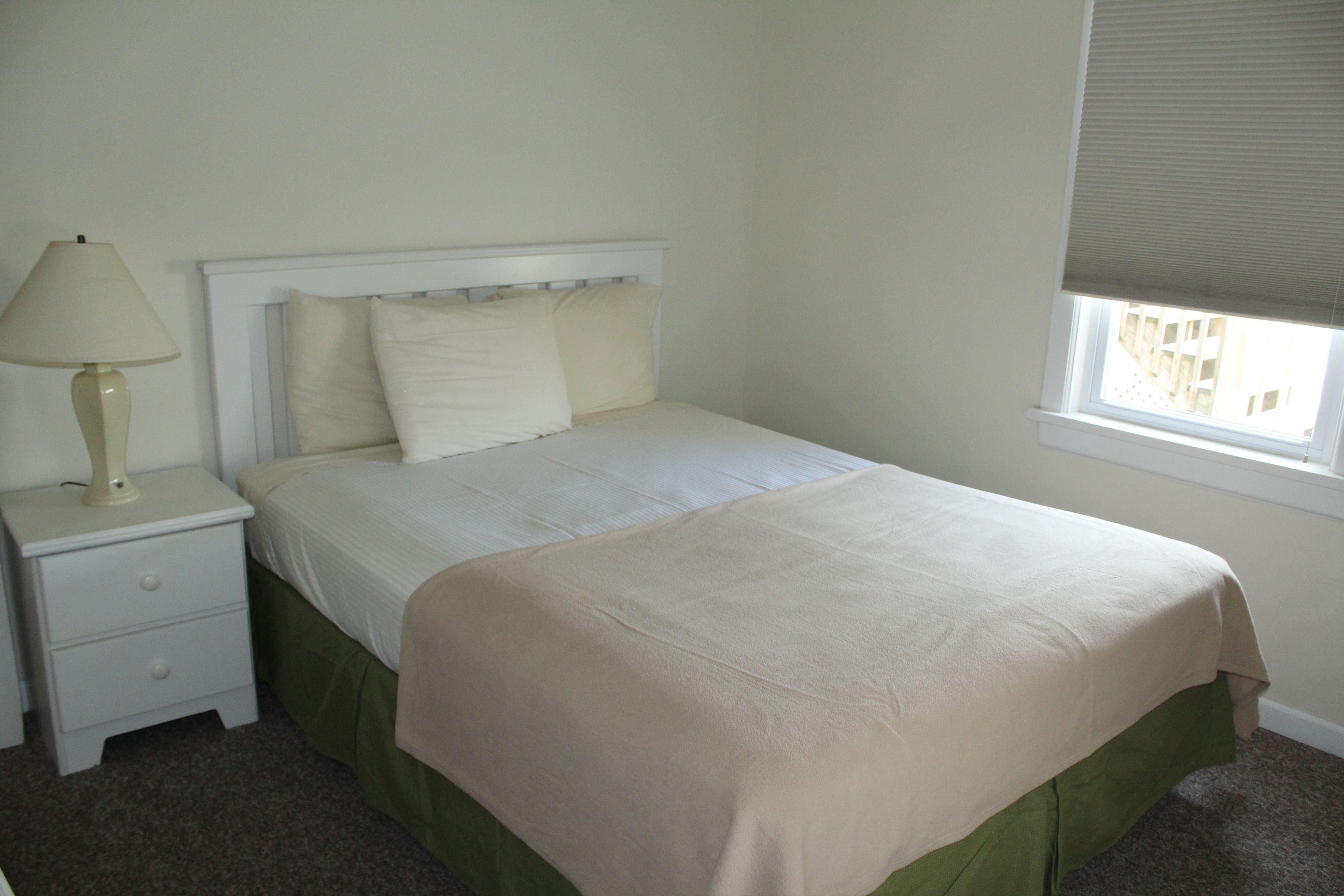 A neatly made bed with a white headboard, a bedside lamp, and a window with blinds.