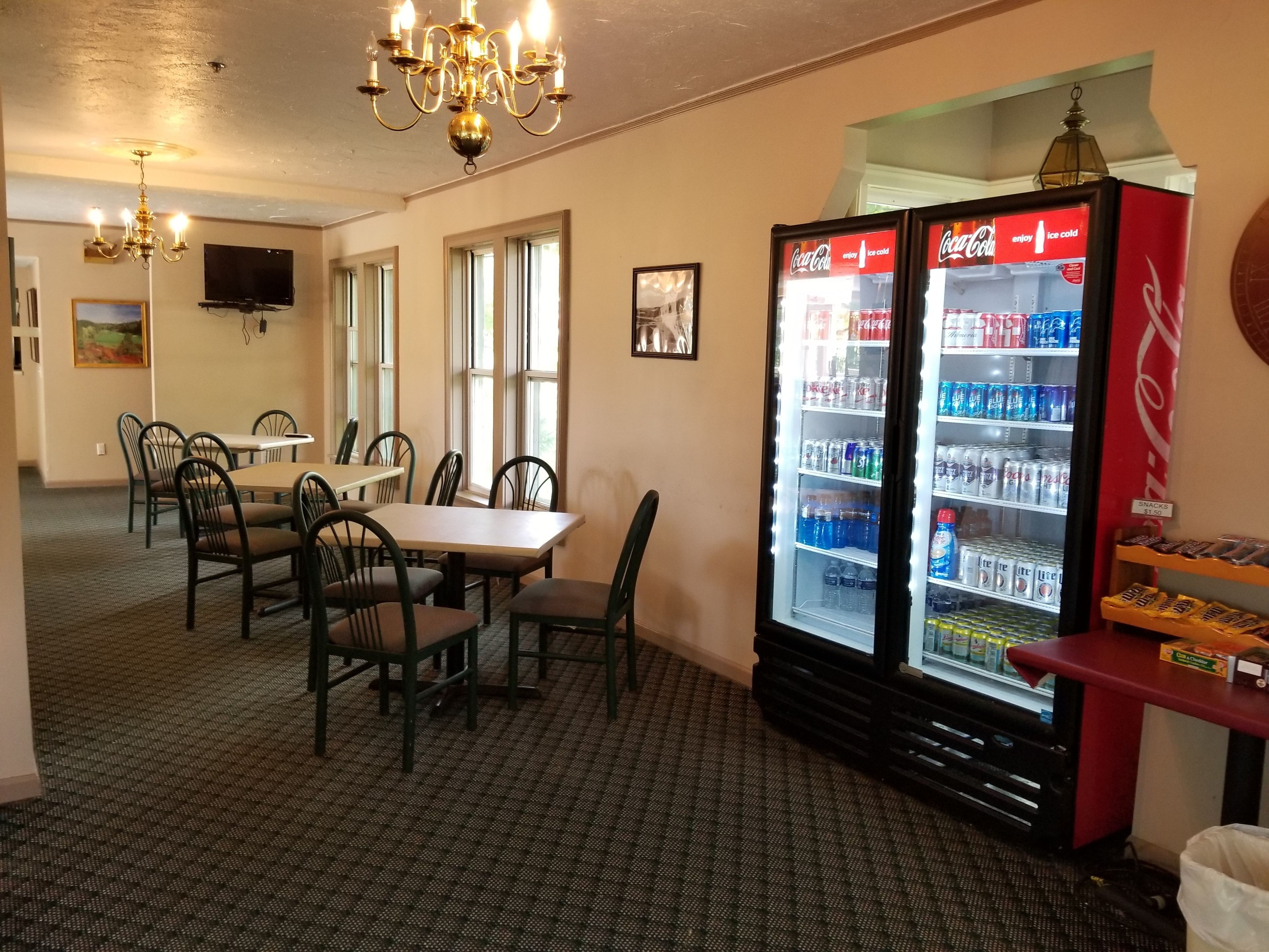 A dining area with a table and chairs, a refrigerator stocked with beverages, and a chandelier.