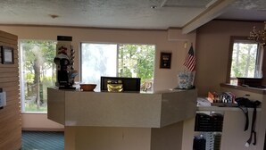 A reception area with a counter, a computer, a framed certificate, and a window with a view of trees. - Dunmaglas Golf Course (Charlevoix)