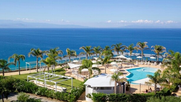 Un resort con piscina, palmeras y vista al océano.