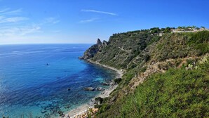 Un paisaje costero con una vista despejada del mar, acantilados rocosos y una colina con edificios.