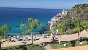 Vista costera con un patio que cuenta con sillas y mesas, con vista al mar y una ladera rocosa.