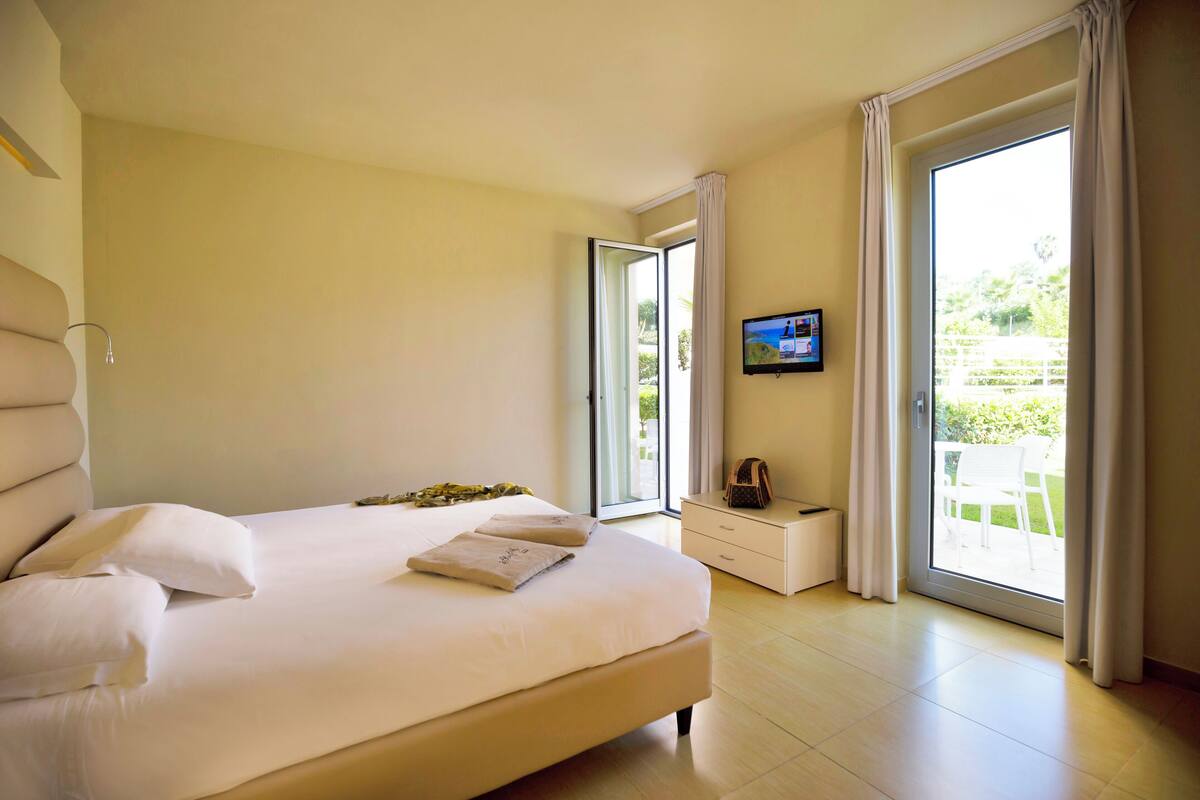 A bedroom with a large bed, a television on the wall, and a sliding glass door to the outside.
