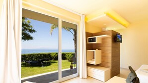 Habitación de hotel moderna con puerta de cristal corredera que da a un balcón con vistas al mar.