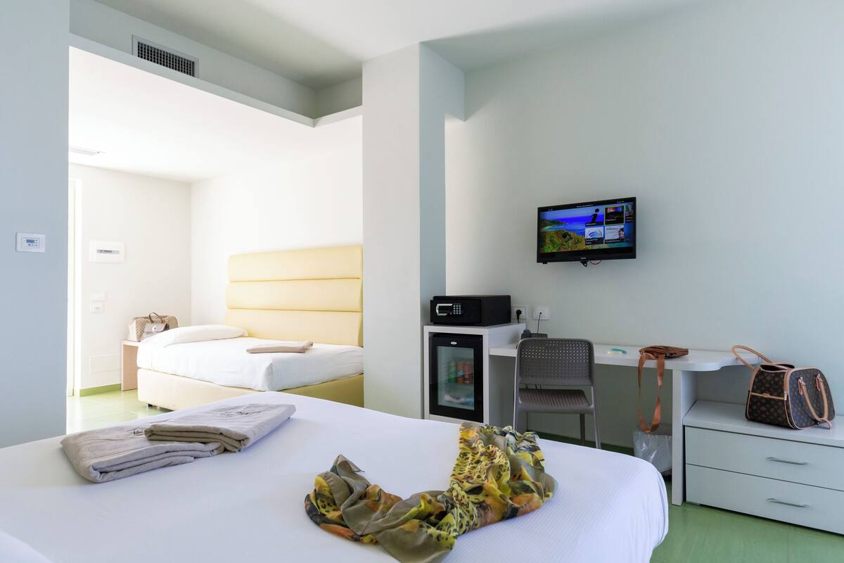 A hotel room with a bed, a desk with a computer, a television, and a chair.