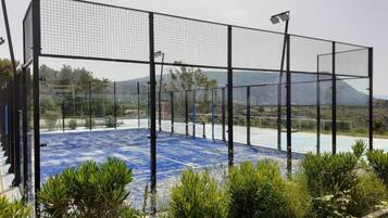 Una cancha de tenis con una red, rodeada por una cerca de metal, y una montaña al fondo.