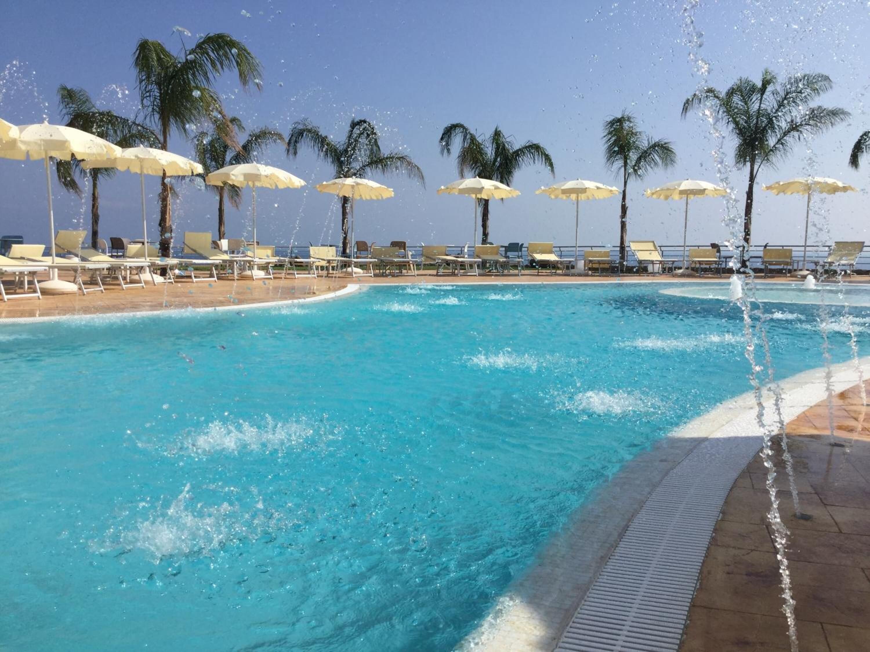 Una piscina con agua azul cristalina, rodeada de sillas de descanso y sombrillas blancas.