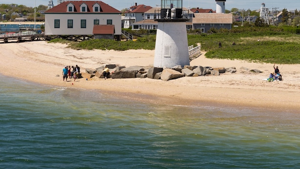 A lighthouse on a sandy beach with a white building in the background. -  76 Main Ink Press Hotel (Nantucket)