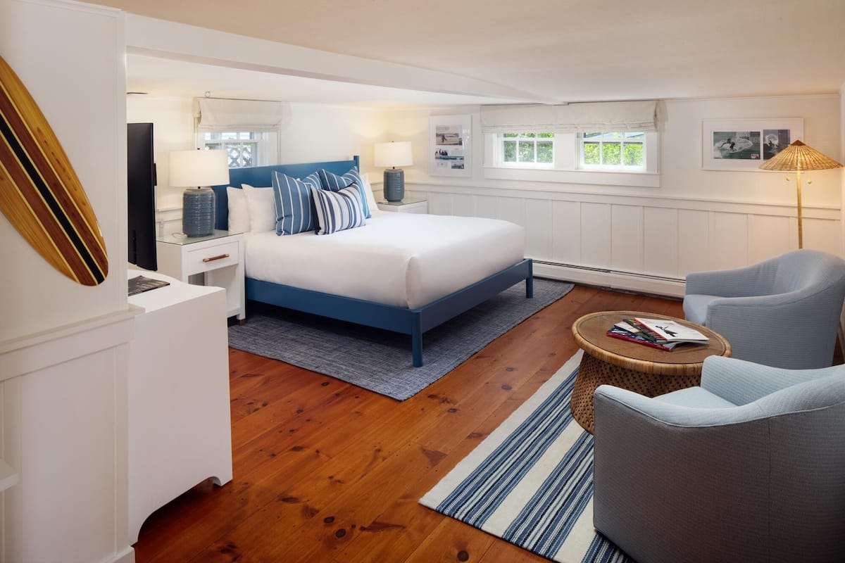 Quarto moderno com cama, mesas de cabeceira, abajur, cadeira e uma pequena mesa.