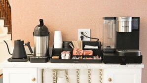 A coffee station with a coffee maker, cups, and coffee pods on a white counter.