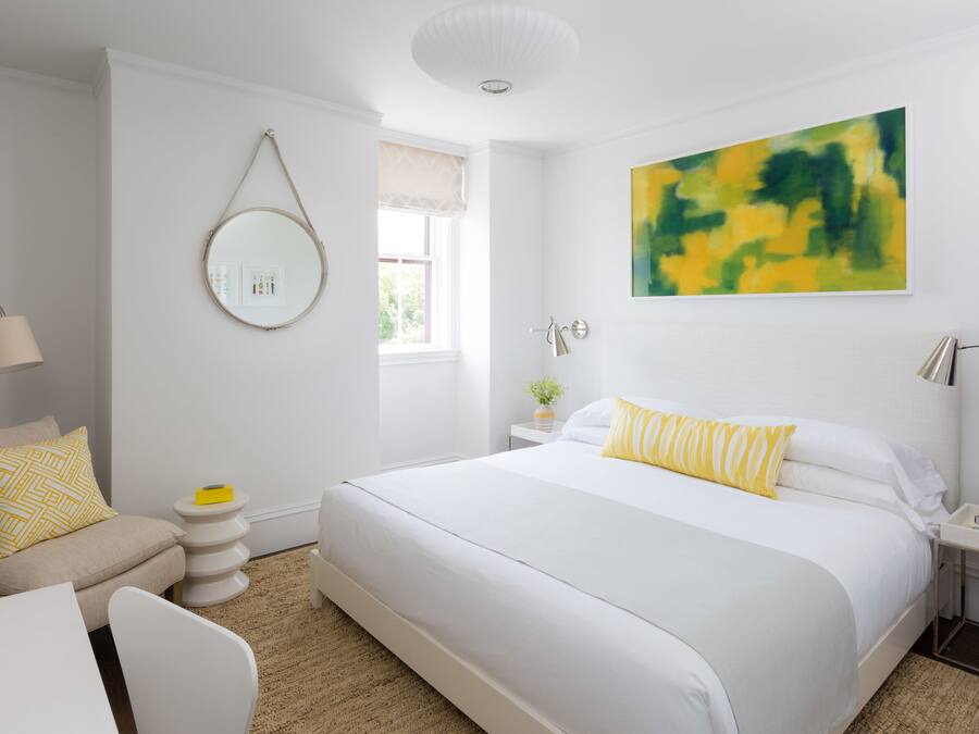 A modern bedroom with a large bed, bedside tables, a round mirror, and a window with a view.