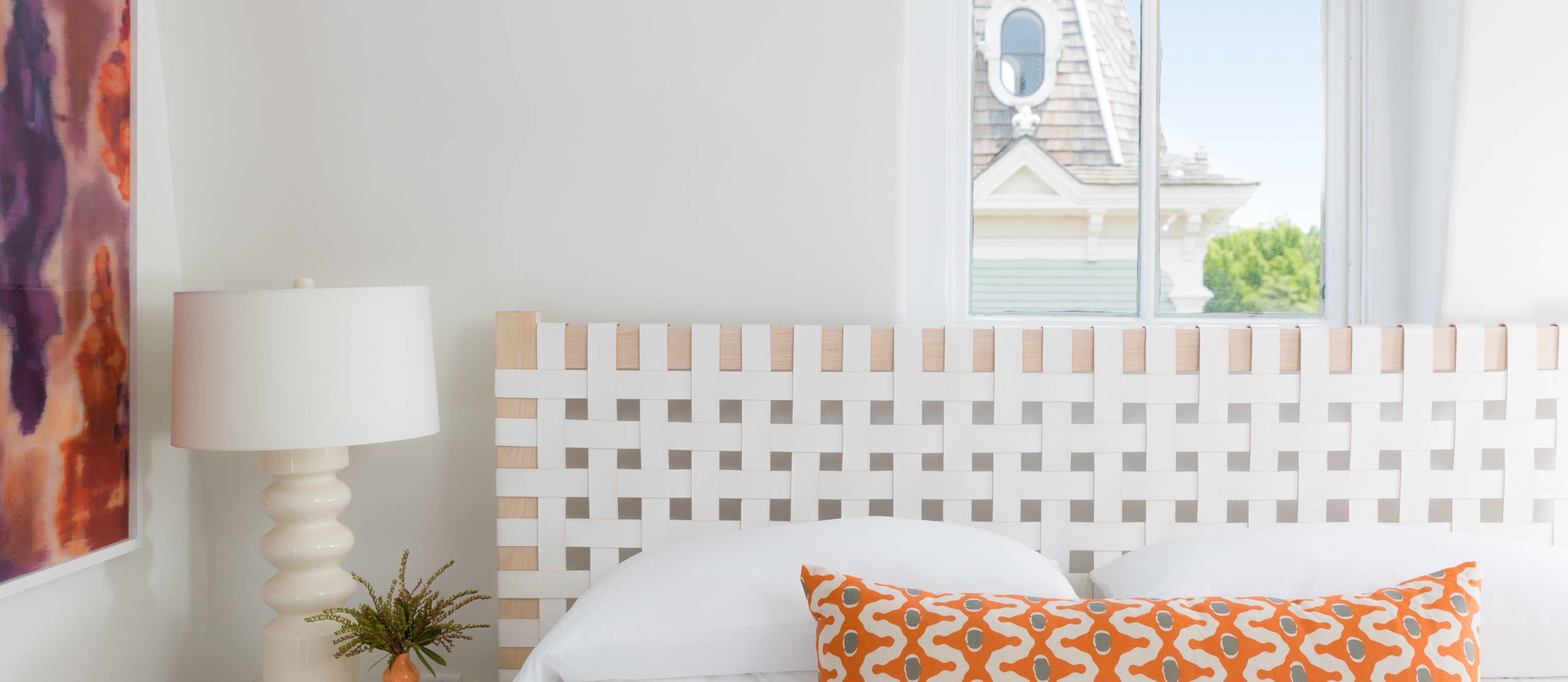 A bedroom with a white headboard, a bedside lamp, and a window with a view of a building.
