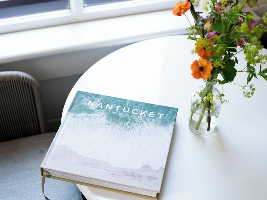 A book titled "NANTUCKET" on a white table with a vase of flowers.
