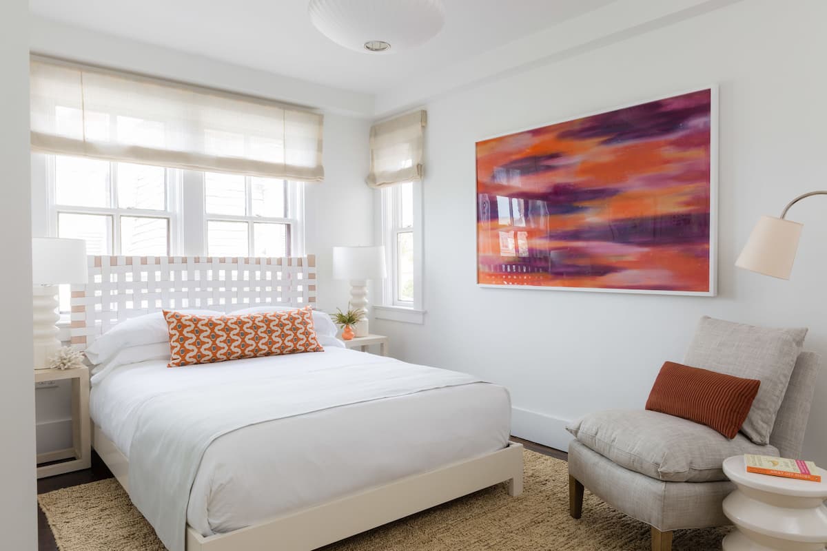 A modern bedroom with a bed, a chair, a nightstand, and a large abstract painting on the wall.