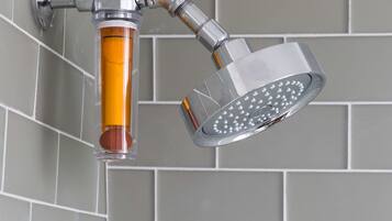 A showerhead with a transparent rain shower attachment and a separate handheld showerhead, mounted on a tiled wall.