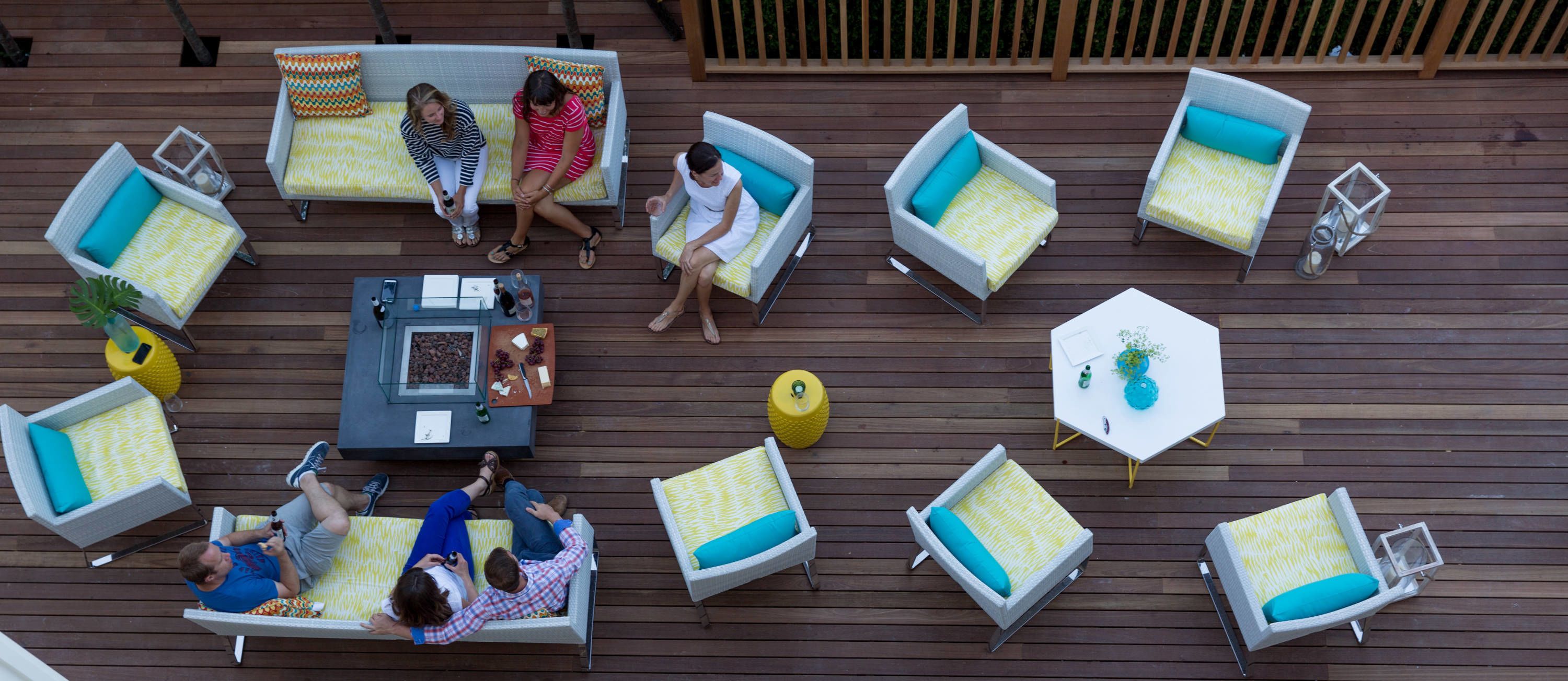 Um terraço ao ar livre com várias áreas de estar, incluindo sofás e cadeiras, dispostas ao redor de uma mesa central com uma garrafa e uma tigela de uvas.