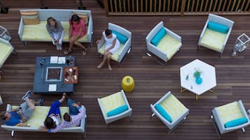 Um terraço ao ar livre com várias áreas de estar, incluindo sofás e cadeiras, dispostas ao redor de uma mesa central com uma garrafa e uma tigela de uvas.