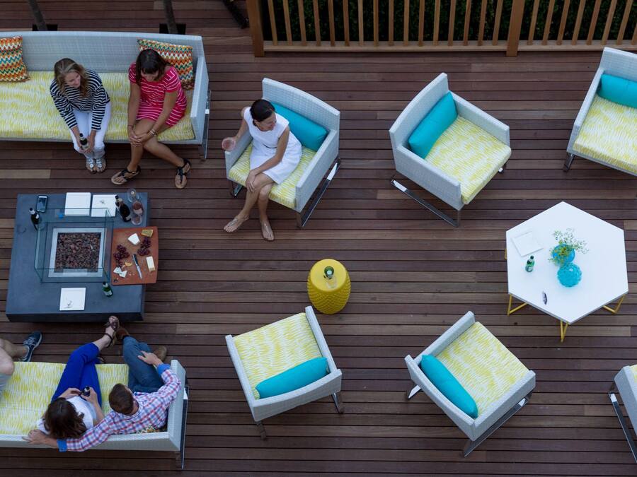 Um terraço ao ar livre com várias áreas de estar, incluindo sofás e cadeiras, dispostas ao redor de uma mesa central com uma garrafa e uma tigela de uvas.