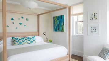 A four-poster bed with a white and blue patterned pillow, a modern abstract painting, and framed botanical prints on the wall.