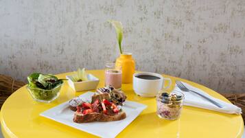 A breakfast table with toast, fruit, a salad, a coffee cup, a juice, and a flower in a vase.