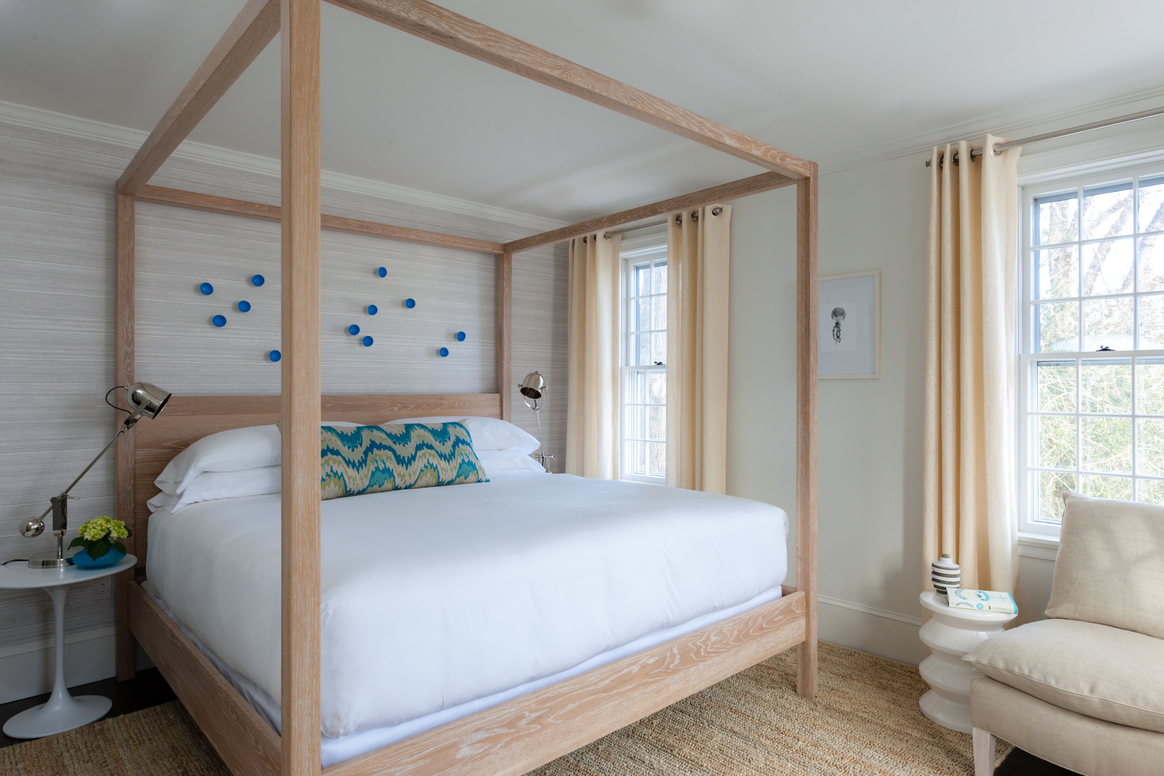 A four-poster bed with a wooden frame, a small bedside table with a lamp, and a chair with a cushion.