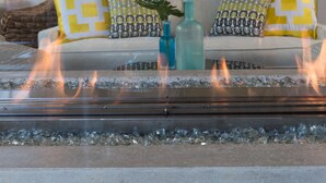 A modern living room with a glass fireplace, a sofa with patterned cushions, and a large window with a view of the outdoors. - 21 Broad Hotel (Nantucket)