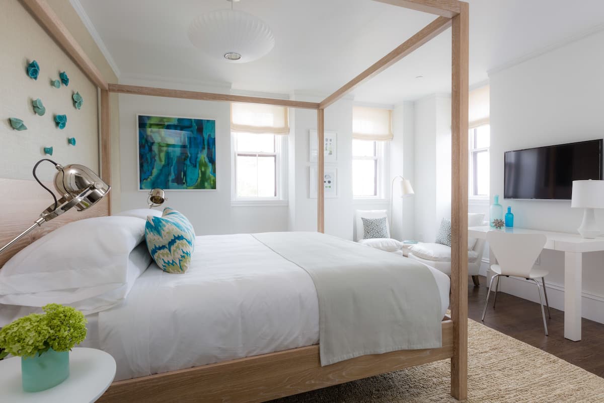 A modern bedroom with a wooden bed frame, a desk, and a TV.