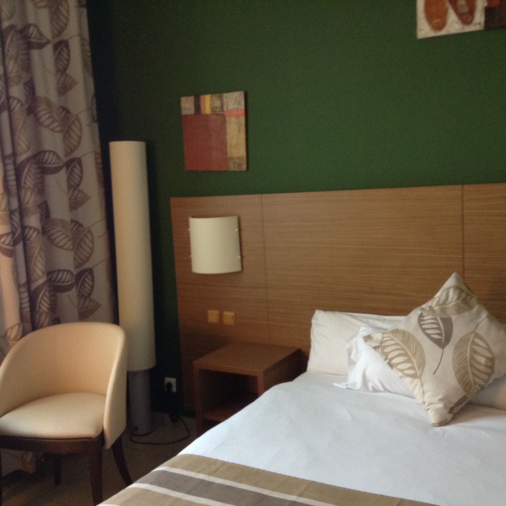 A hotel room with a bed, a chair, a nightstand, and a wall art piece.