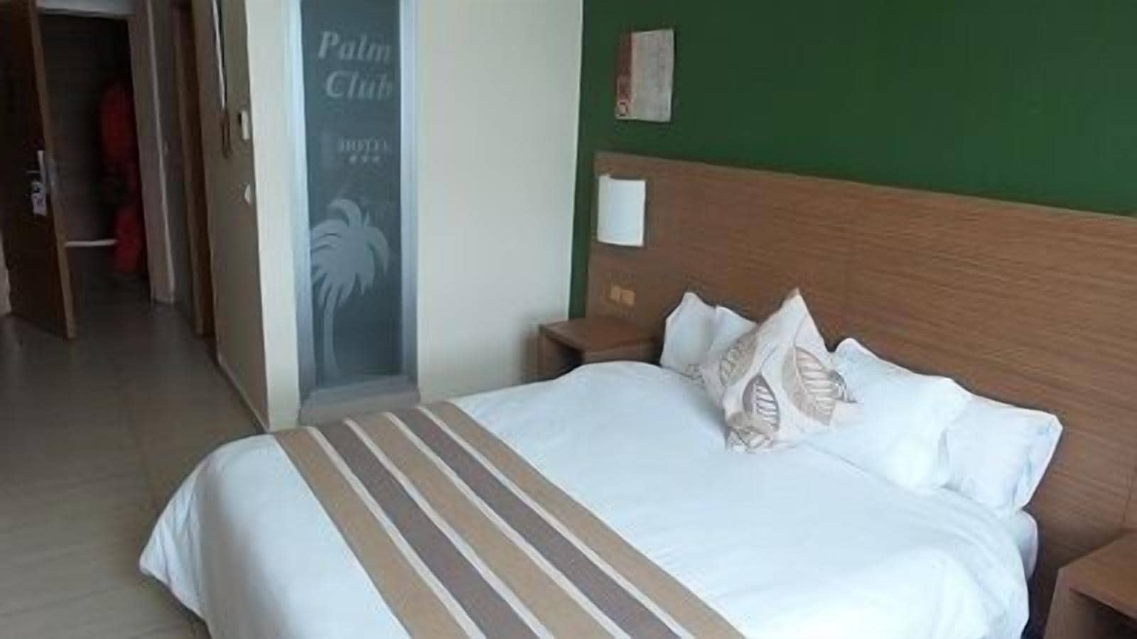 A hotel room with a large bed, a wooden headboard, and a green wall.