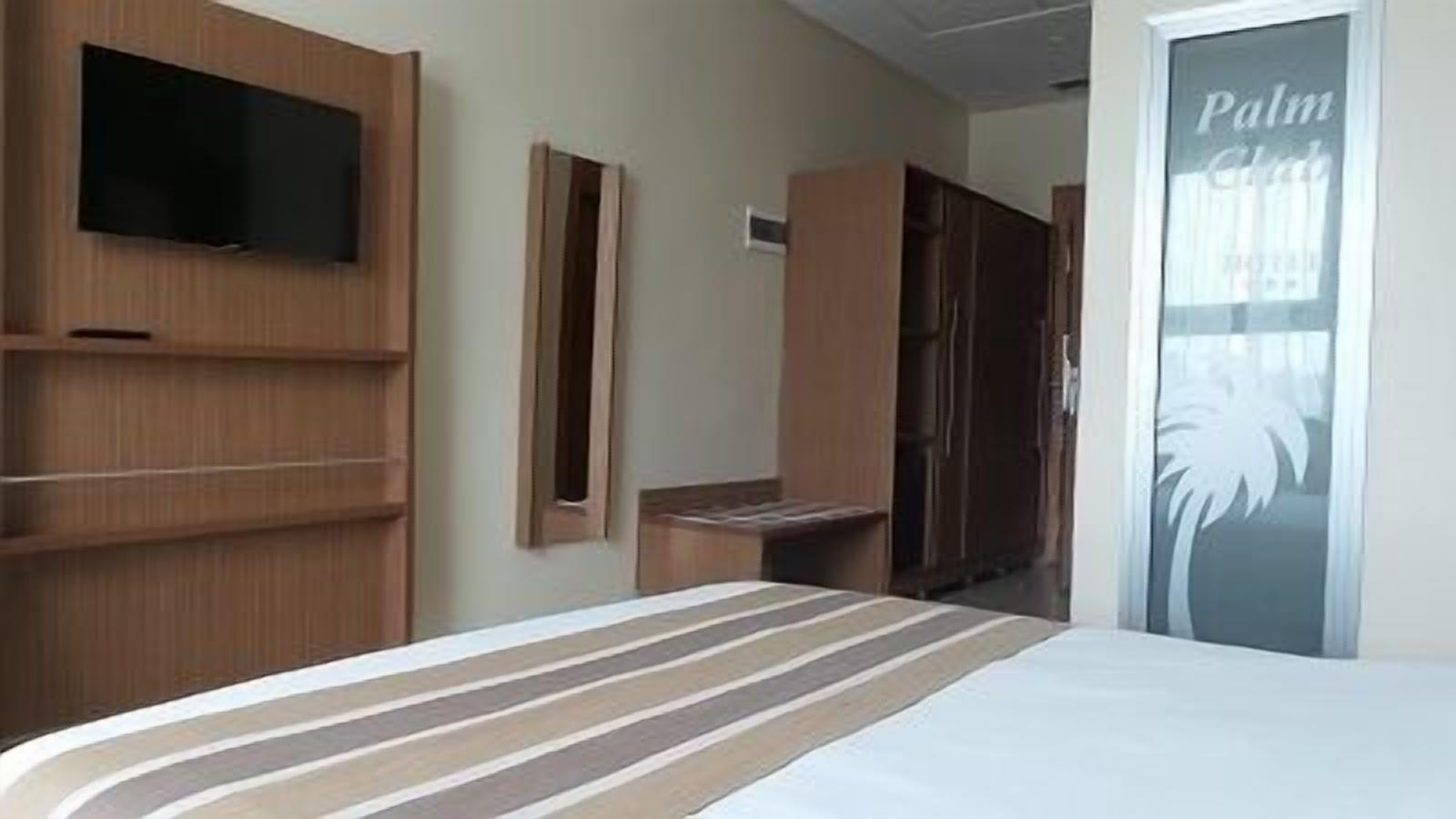 Une chambre d’hôtel avec un lit, une armoire en bois, un téléviseur et une porte ornée d’un motif de palmier.