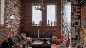 A cozy living room with a brick wall, a leather sofa, a wooden ottoman, a red chair, a floor lamp, and a wall of photographs. - The Bow Hotel (Portsmouth)