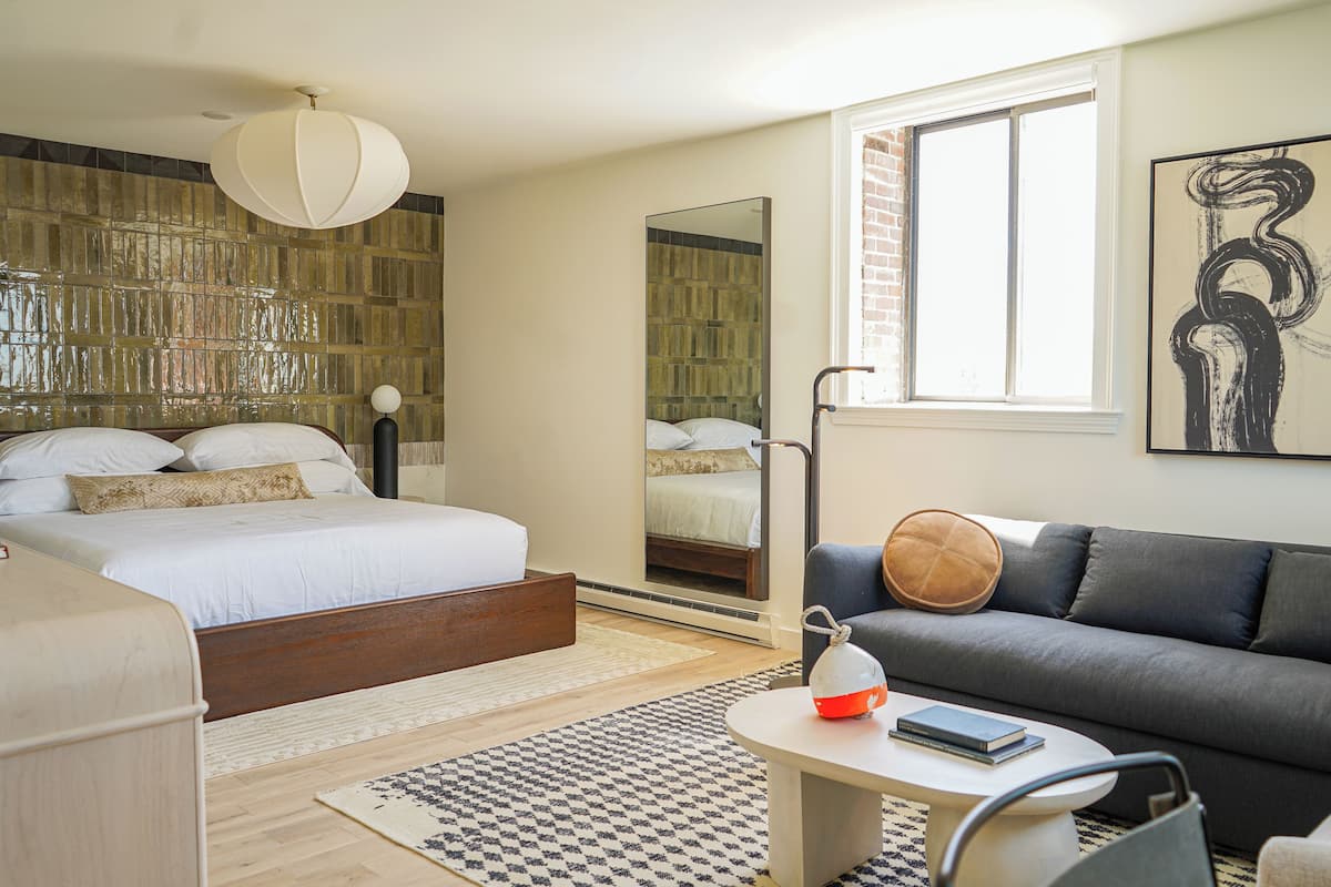 A modern bedroom with a large bed, a sofa, a coffee table, and a mirror.
