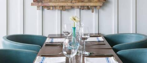 A dining area with a wooden table set for two, teal upholstered chairs, and a wall-mounted artwork depicting a figure in a dynamic pose.