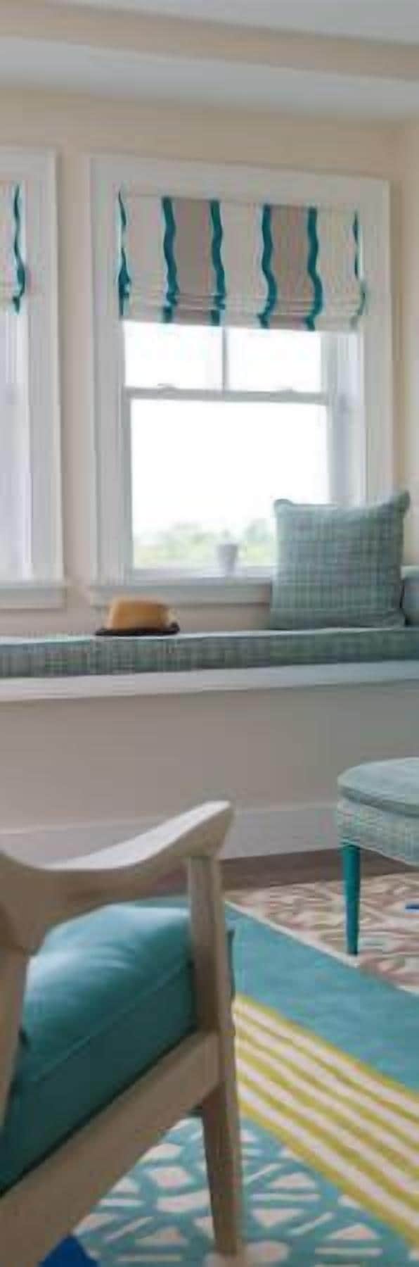 Una habitación con un asiento junto a la ventana, una silla y un tapete estampado.