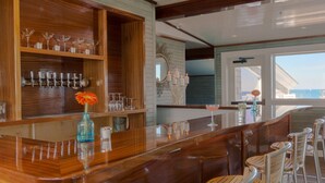 Un espace bar avec des étagères en bois, des tabourets de bar et une vue sur l’océan.