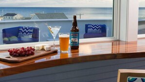 Un coin bar avec vue sur l’océan, une bouteille de bière, un verre de bière et une assiette de raisins.