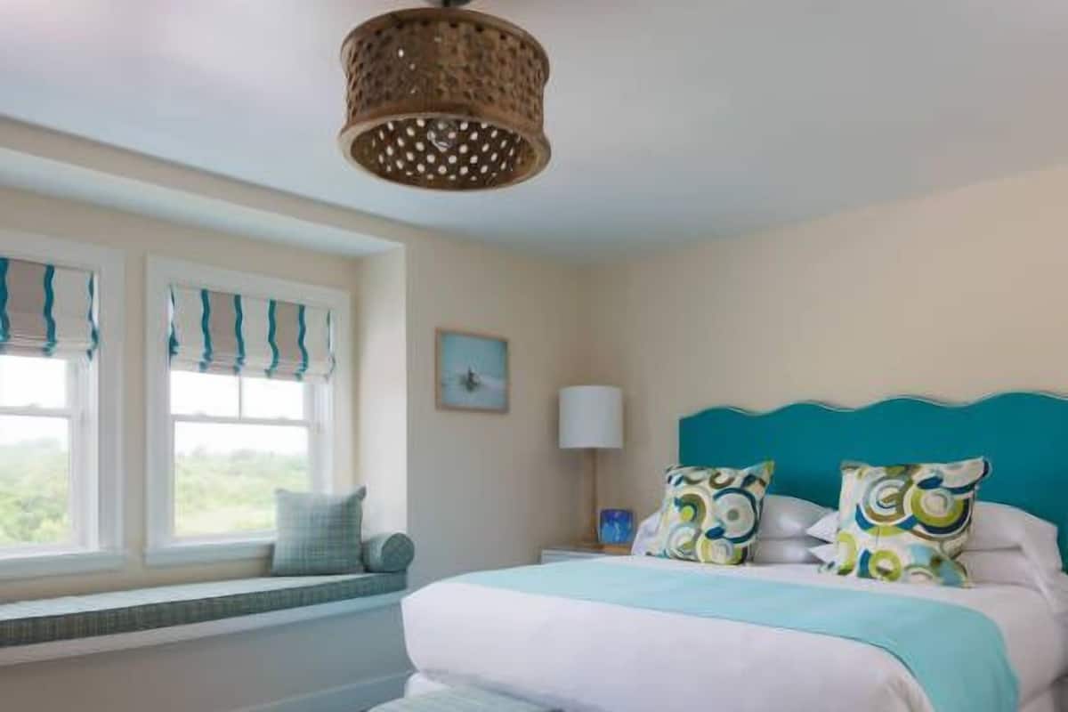 A bedroom with a large bed, a window with a view, a bedside table, and a lamp.