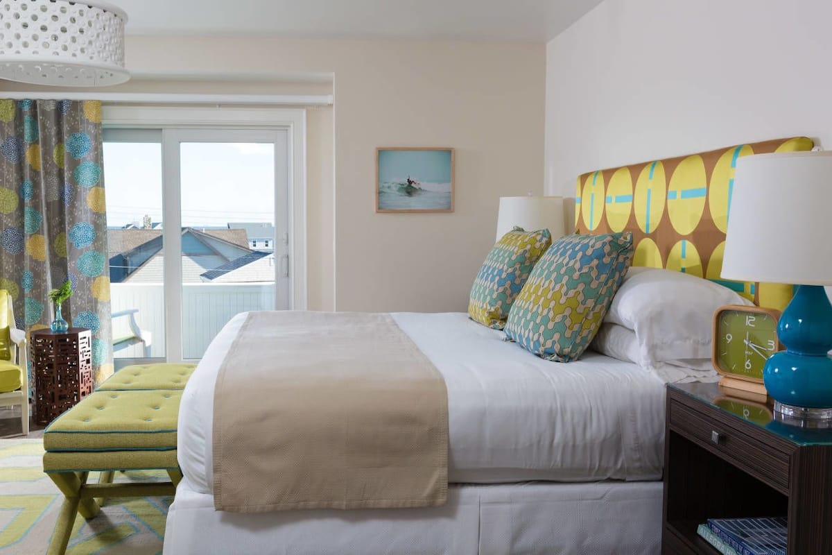 A hotel room with a bed, a chair, a lamp, and a painting on the wall.