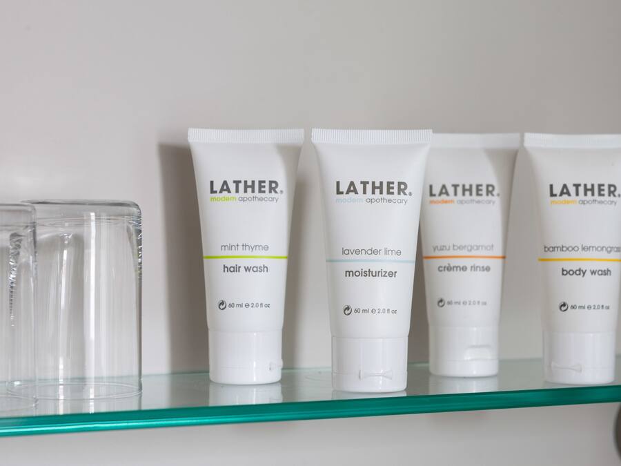 A shelf with five Lather modern apothecary products: hair wash, moisturizer, creme rinse, and body wash.