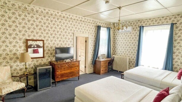 A hotel room with two beds, a TV, a dresser, a desk, and a radiator. - Brandon Inn (Brandon)