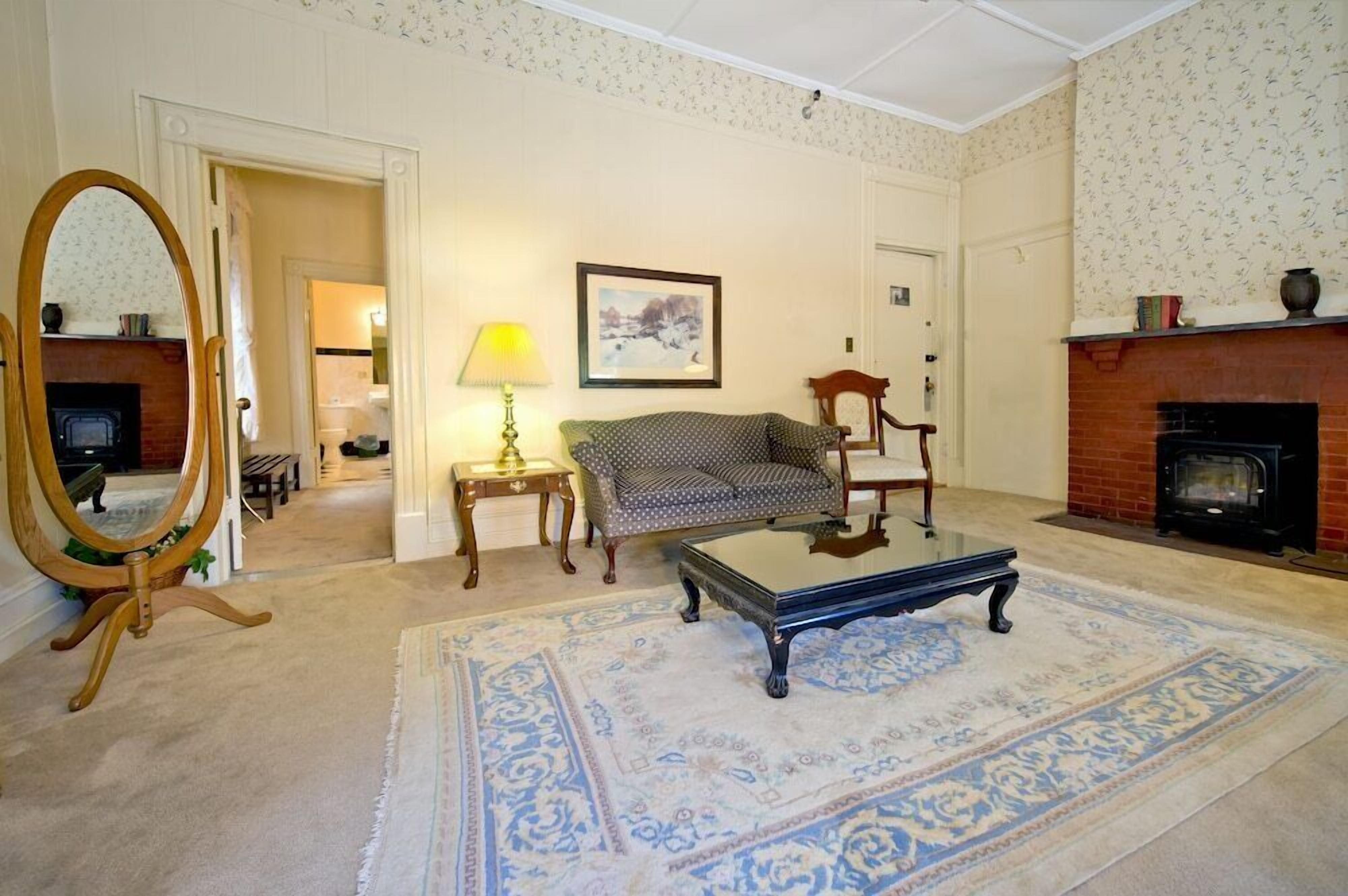 A room with a fireplace, a sofa, a coffee table, a mirror, and a patterned rug.