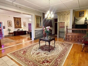 A spacious lobby with a wooden floor, a chandelier, an American flag, and a reception desk.